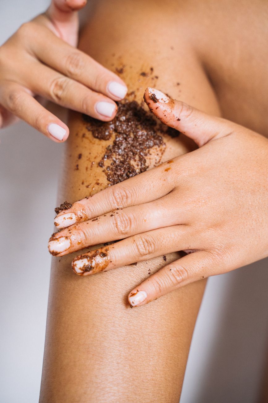 gros plan des mains appliquant un gommage au cafe sur une jambe pour les soins de la peau