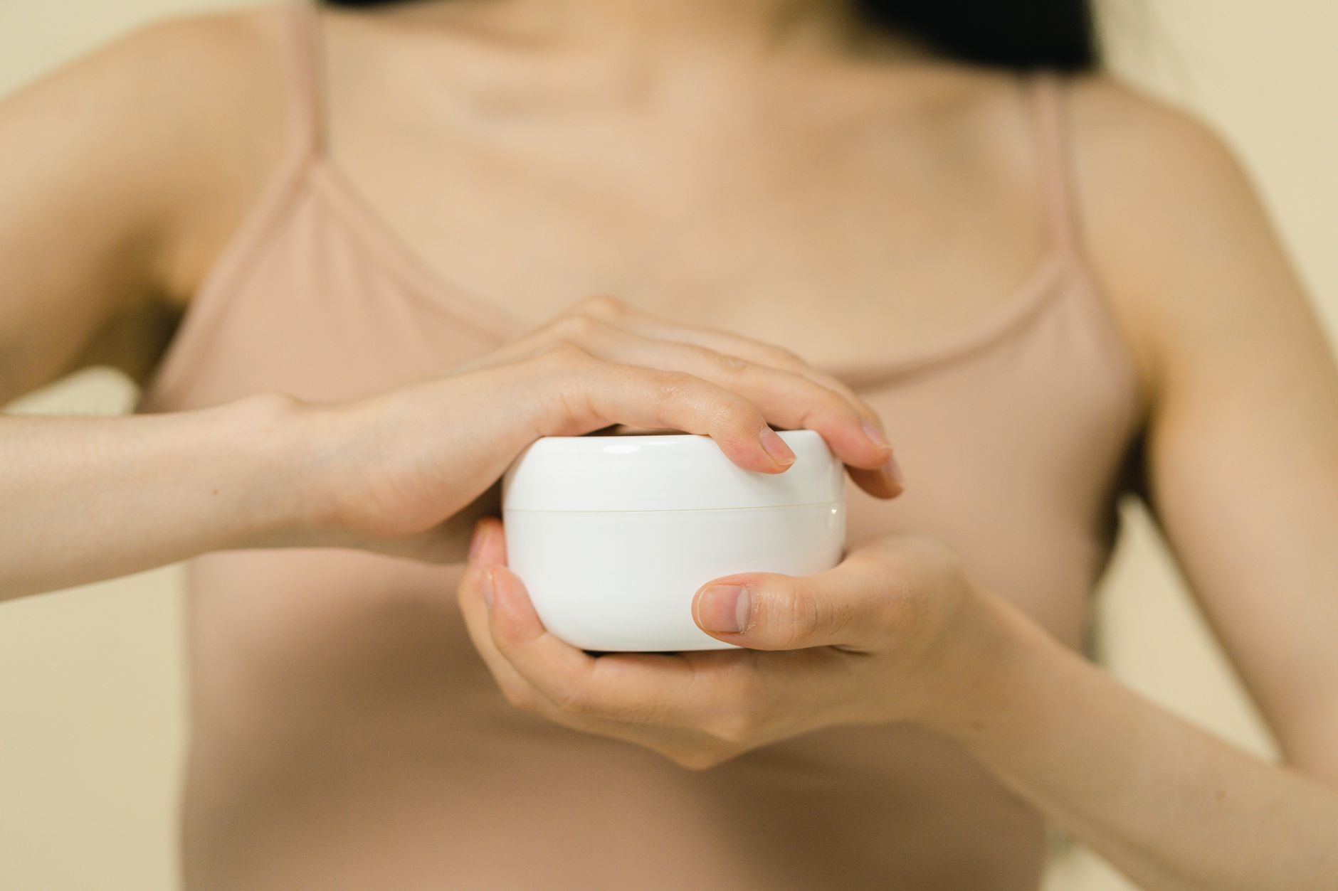 gros plan d une femme appliquant une creme hydratante avec un accent sur ses mains et le contenant de la creme