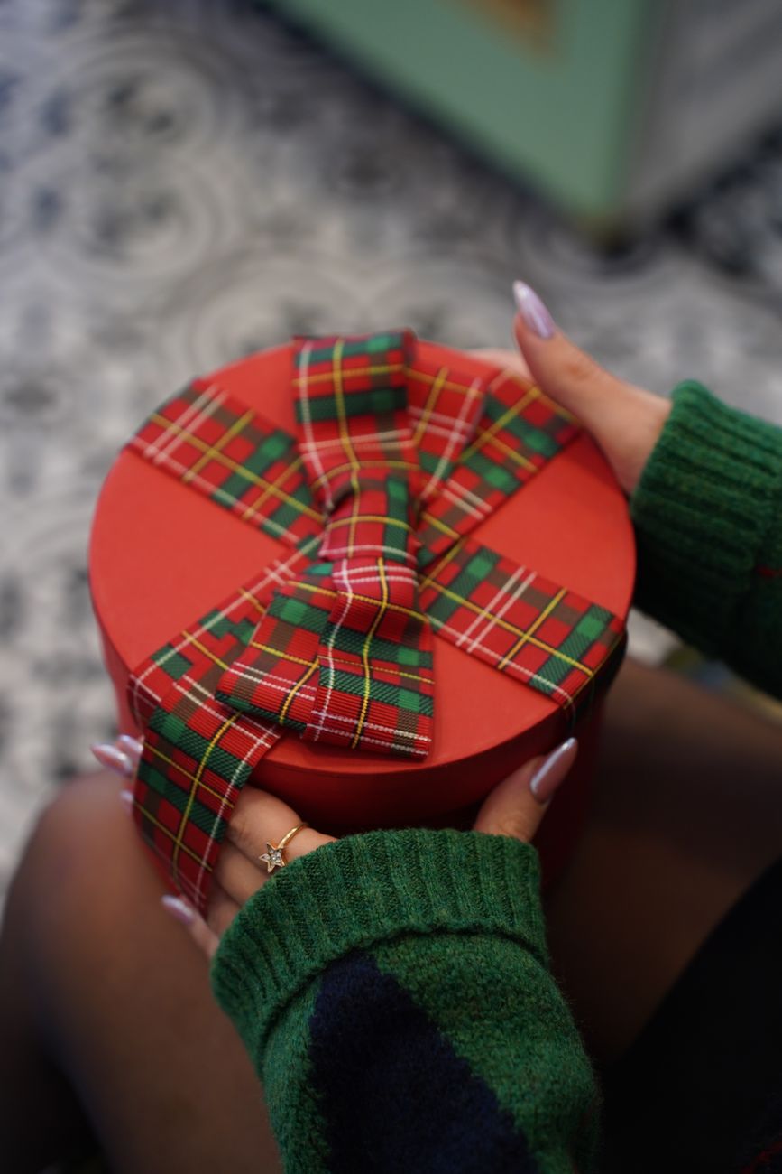 une boite cadeau rouge avec un ruban tartan a carreaux tenue dans les mains parfaite pour noel ou les occasions festives