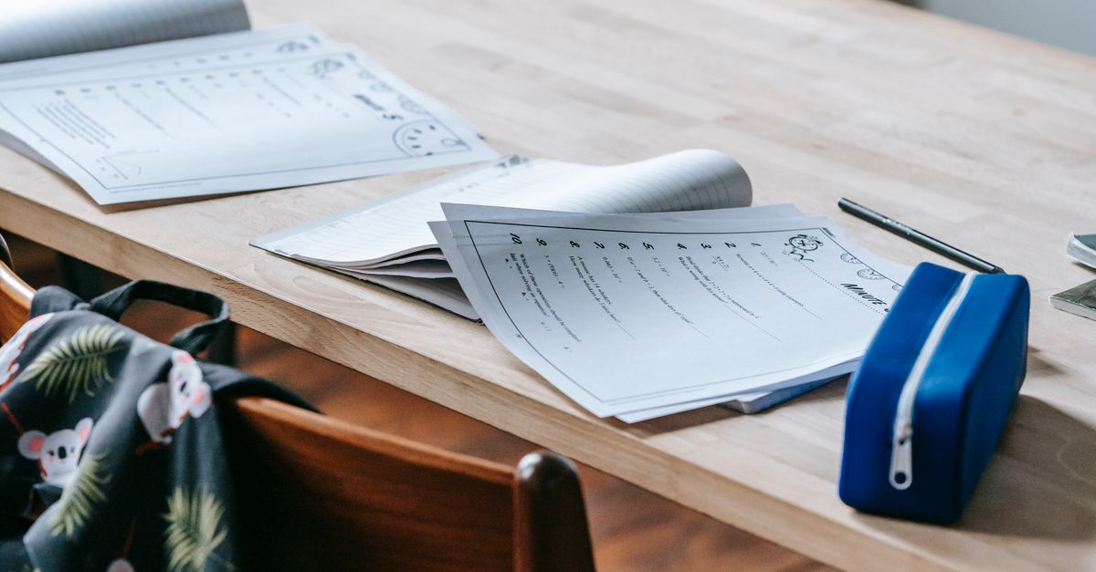 gros plan sur des documents d etudes sur un bureau en bois dans un environnement de classe avec un sac a dos et une trousse