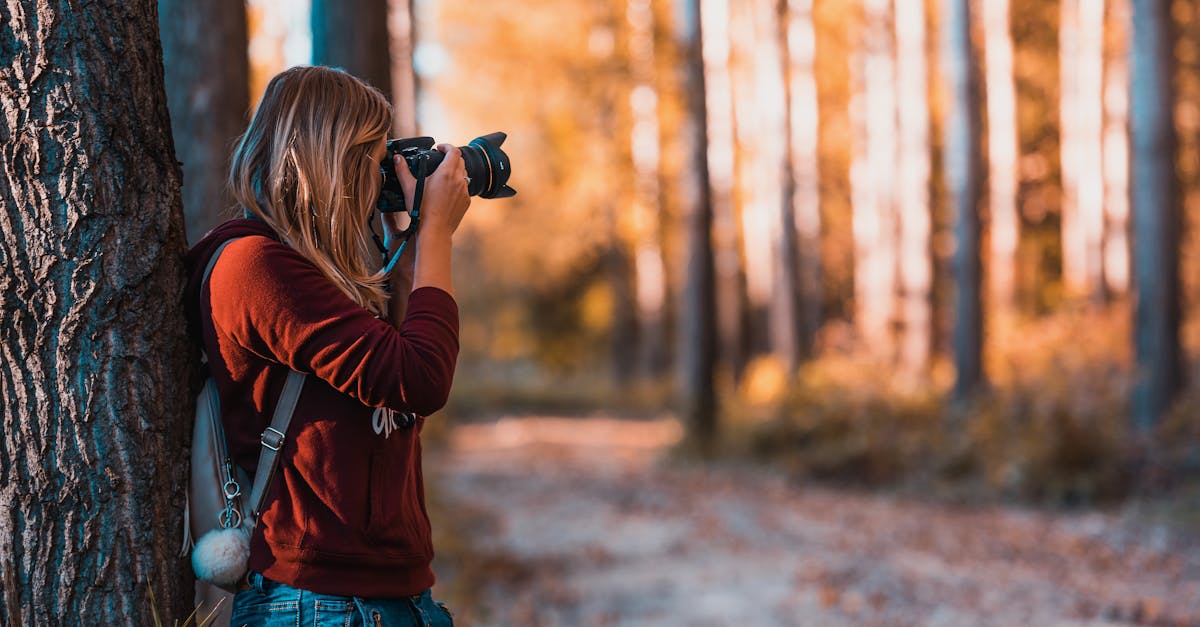 femme se penchant en arriere sur le tronc d arbre a l aide de l appareil photo reflex numerique noir pendant la journee