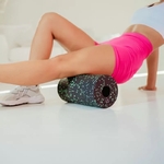 femme-en-short-rose-faisant-un-automassage-avec-un-rouleau-noir-et-vert-sur-sa-jambe