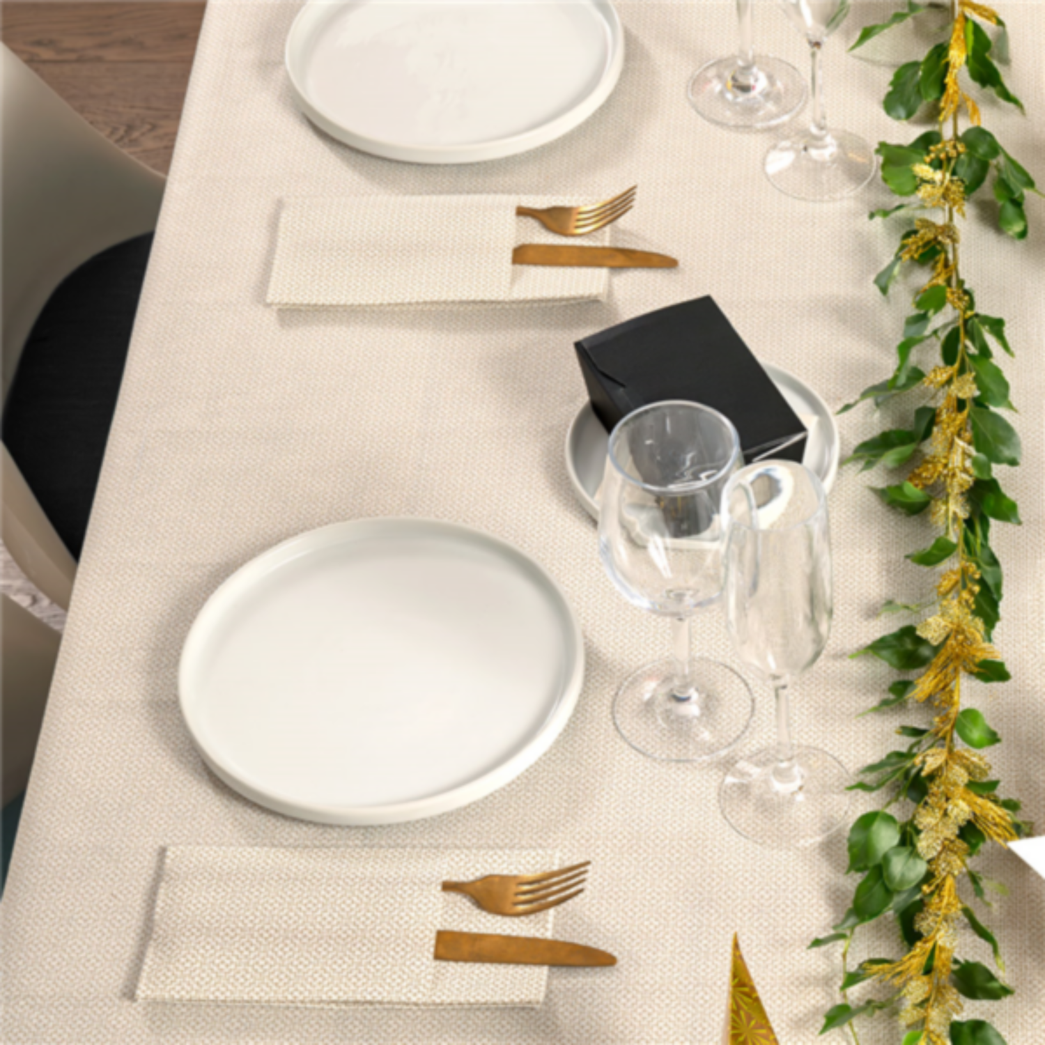 Table de fêtes dressée avec la nappe blanche à motif doré, assiettes, couverts et décorations