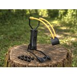 Lance-pierre compact posé sur une souche en forêt avec 8 billes ABS noires.