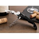 Tire-bouchon sommelier noir utilisé pour l’ouverture d’une bouteille de vin rouge sur table en bois avec bouchons de liège.