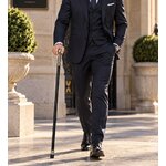 Homme élégant en costume marchant avec une canne Gentleman Luxe noire et argentée devant un bâtiment prestigieux.