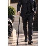 Homme élégant en costume tenant une canne cobra noire et argentée devant un bâtiment prestigieux.