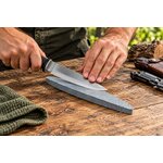 Homme utilisant une pierre daffûtage grise pour aiguiser un couteau outdoor sur une table en bois.