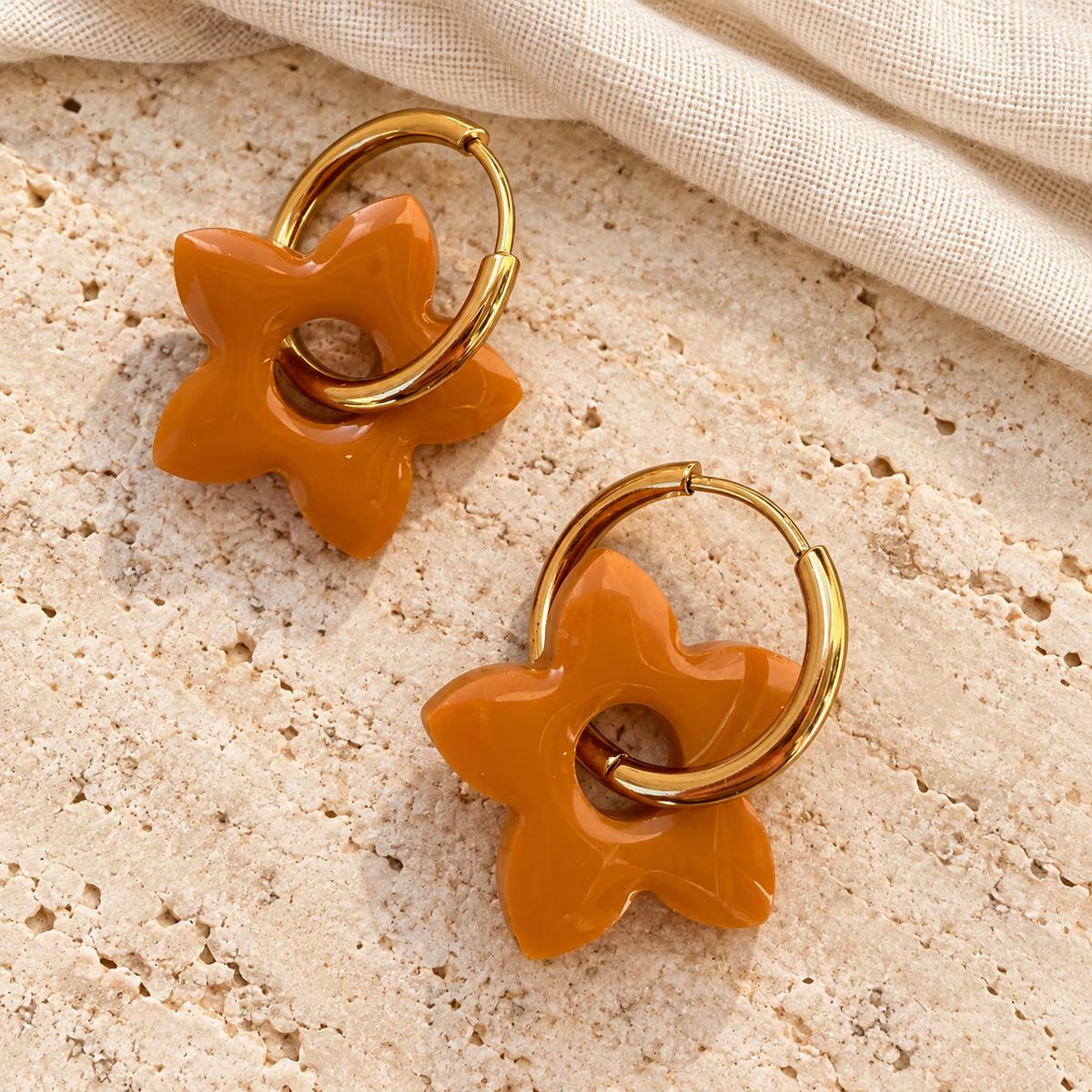 Fleurs de tiaré camel avec créoles dorées sur travertin clair et lin ivoire