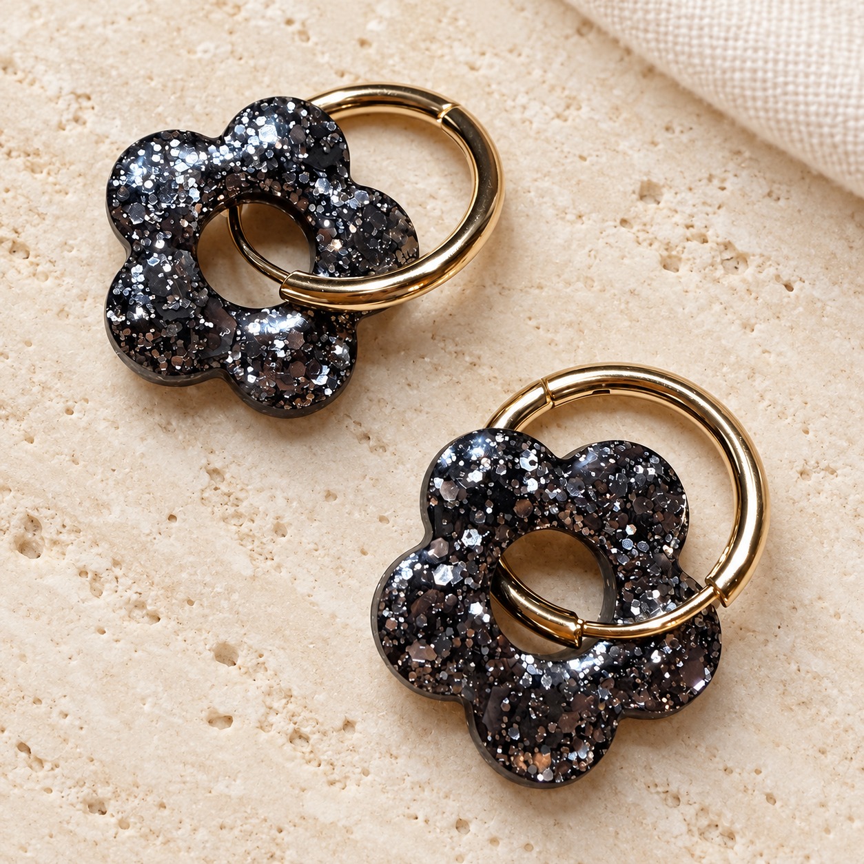 Boucles d’oreilles fleurs noir mix or, référence 029, avec créoles dorées sur travertin clair.
